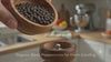 Fresh organic black peppercorns being ground and sprinkled over hot food in a premium kitchen setting.